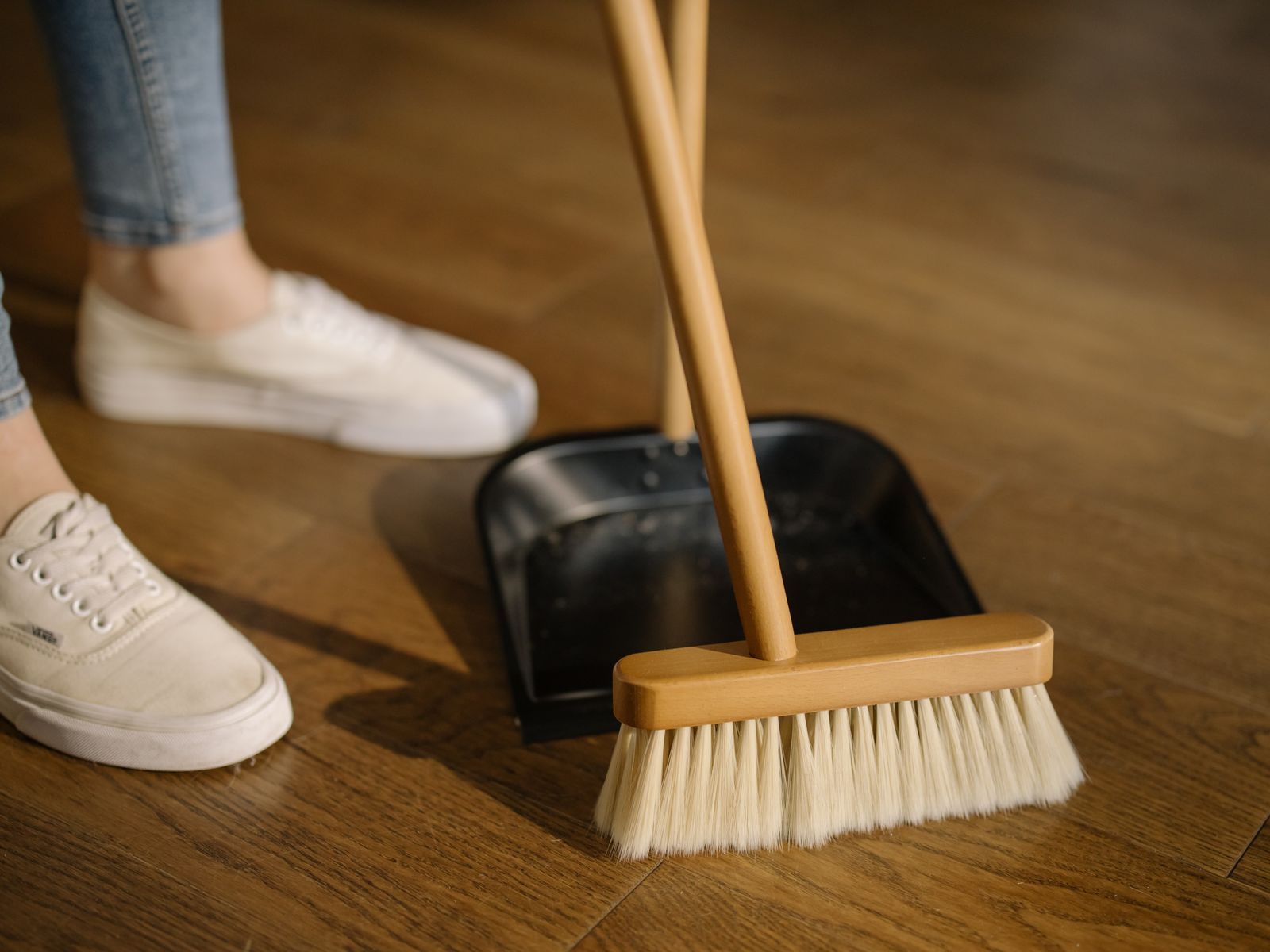 Broom and dustpan mid sweep on a warm wooden floor