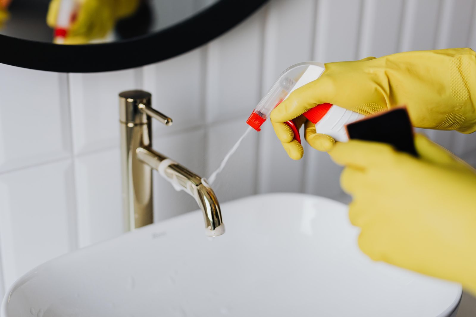 Gloved hands detailing a bathroom faucet during a Moraes deep clean